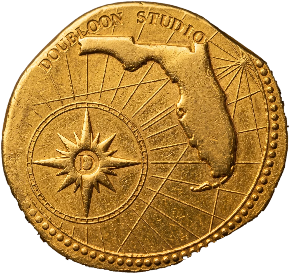 A hand-struck gold coin stamped with a compass rose, the outline of Florida and the words Doubloon Studio.